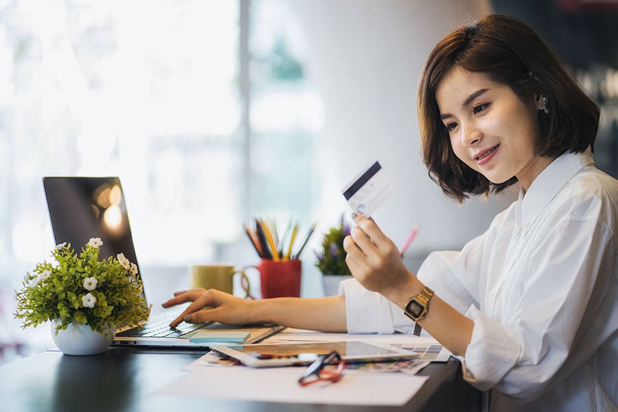 A young woman and first-time credit cardholder makes a purchase on her laptop while holding her credit card.