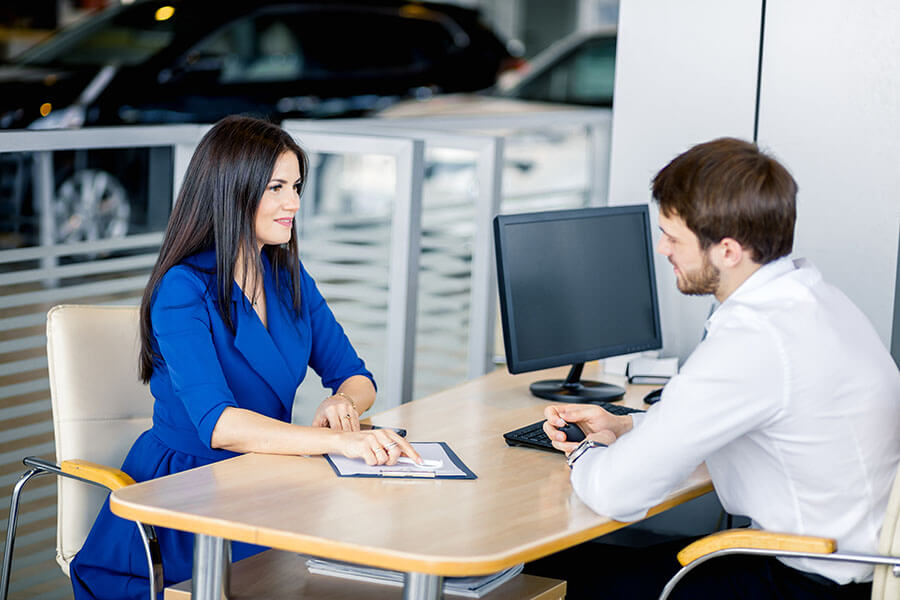 a man signs paperwork with a saleswoman at the dealership after determining his ideal auto loan term